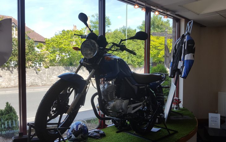 A blue motorcycle in a window display, surrounded by helmets and jackets.