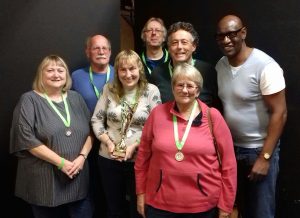 6 people pictured wearing medals and holding a trophy for winning the quiz.