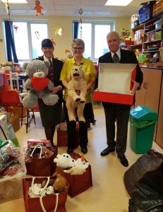 3 colleagues from Bexley standing each holding a grey teddy, a stuffed dog and a red open box.