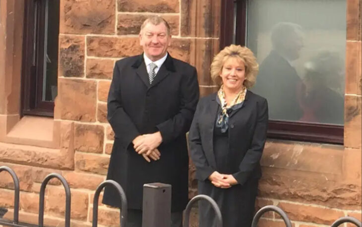 Owners of Sim & Son Funeral Directors pictured in front of brick wall.