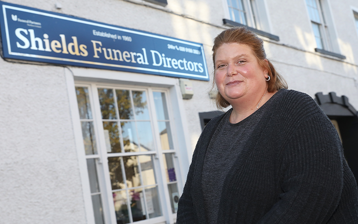 Women stands in front of window with a sign above that reads Shields Funeral Directors.