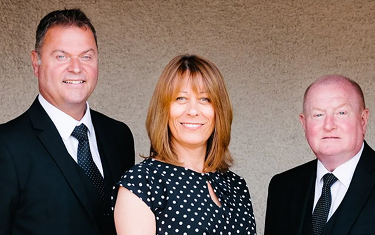 3 people posing for a photo in front of a white wall.