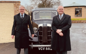 Two men standing in front of a black old fashioned car.