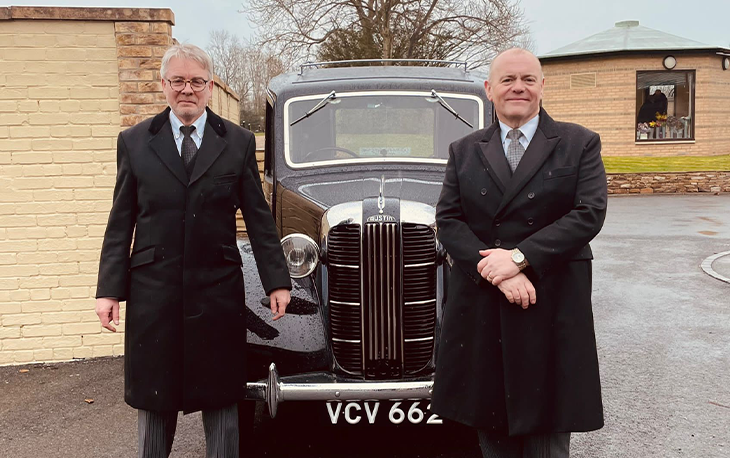 Two men standing in front of a black old fashioned car.
