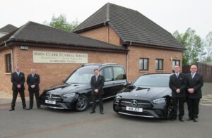 New black hearse and limousine pictured in front of John Clark Funeral Service in Bellshill. Pictured also in front of the cars, 5 funeral staff.