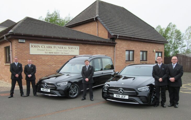 New black hearse and limousine pictured in front of John Clark Funeral Service in Bellshill. Pictured also in front of the cars, 5 funeral staff.
