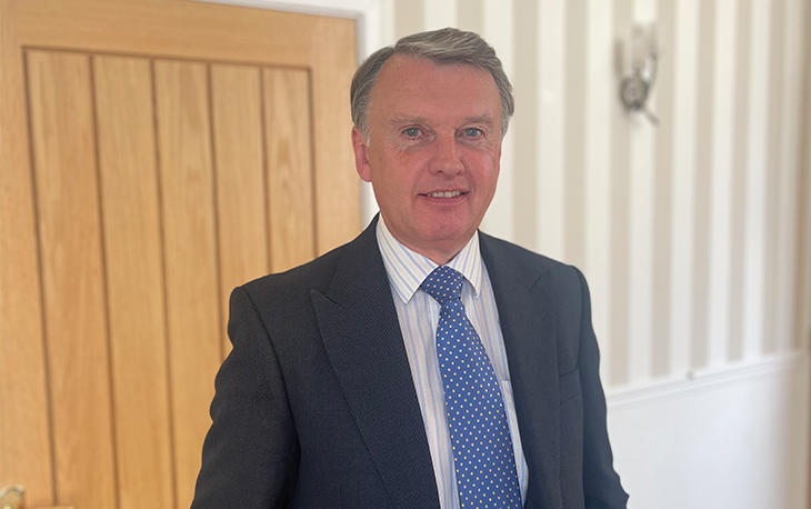 Man standing in front of wooden door wearing a blue suit with light blue tie.