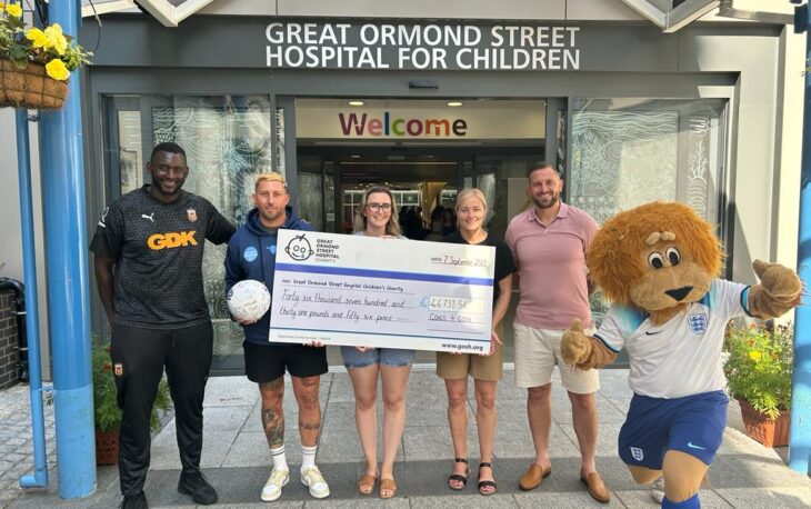 4 people standing in front of Great Ormond Street Hospital. They are holding a large cardboard cheque for £46,731.51 for charity.
