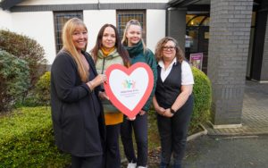 A group of women holding a heart shaped sign for the Community Assistance Programme.