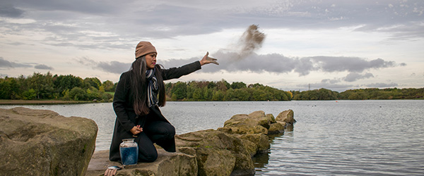 Widow with urn releases ashes into the air over a lake
