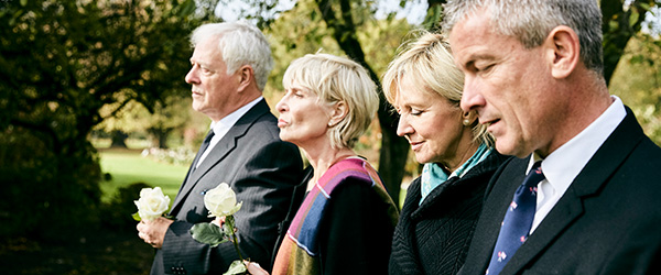 Mourners at a funeral holding white roses