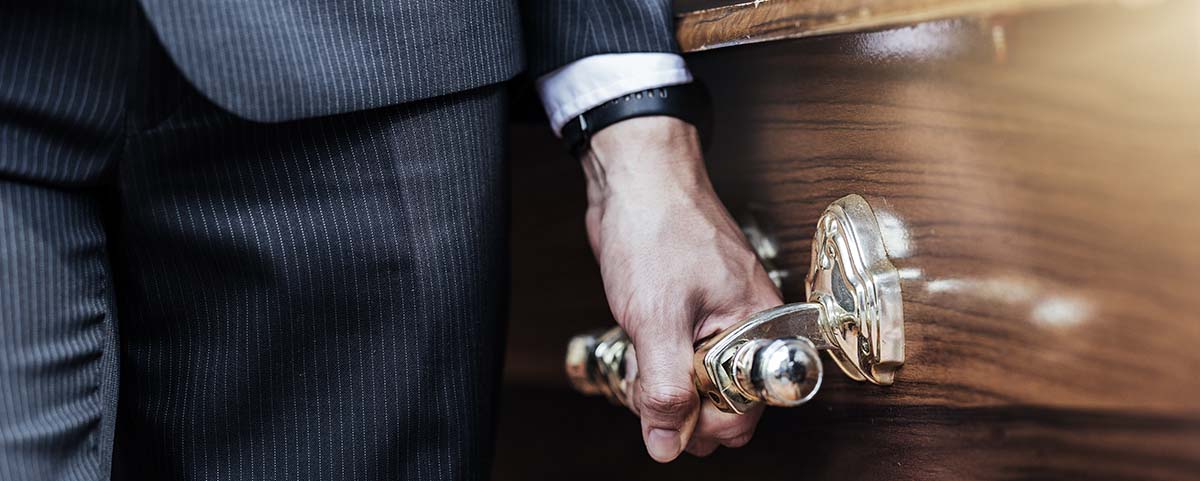 Pallbearer wearing a black suit holding a gold handle on a coffin