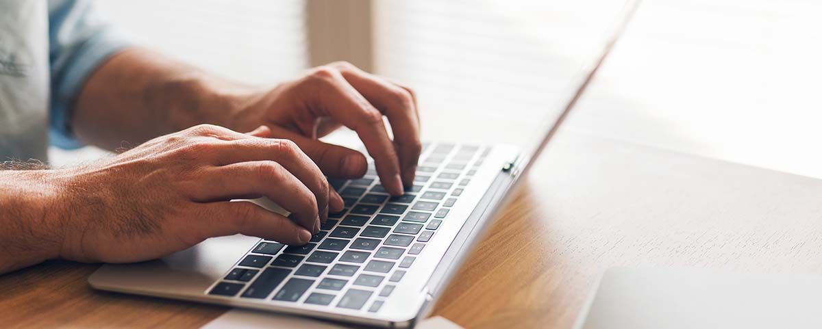 a man's hands typing on a silver laptop