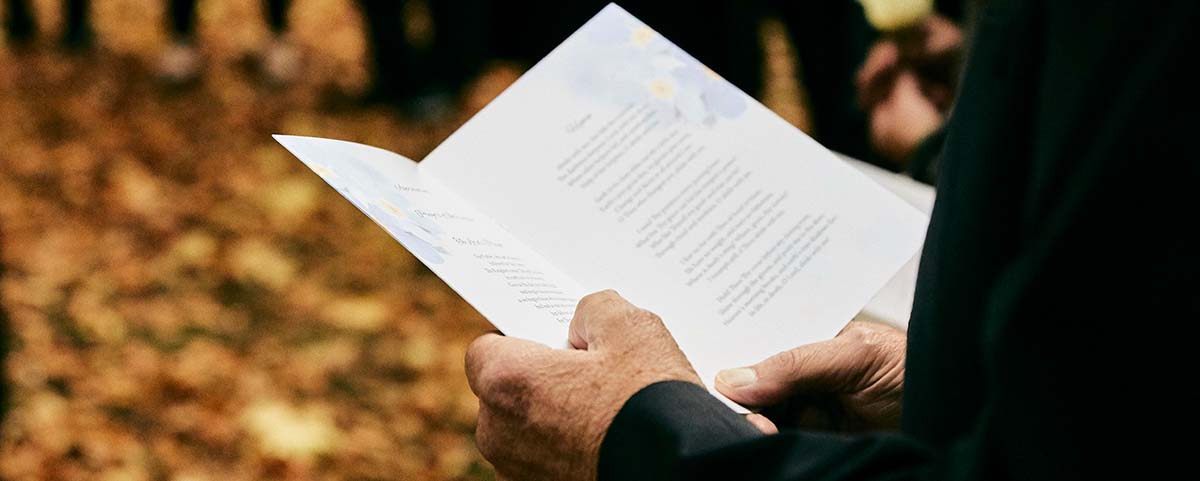 Elderly hands holding an order of service booklet at a funeral